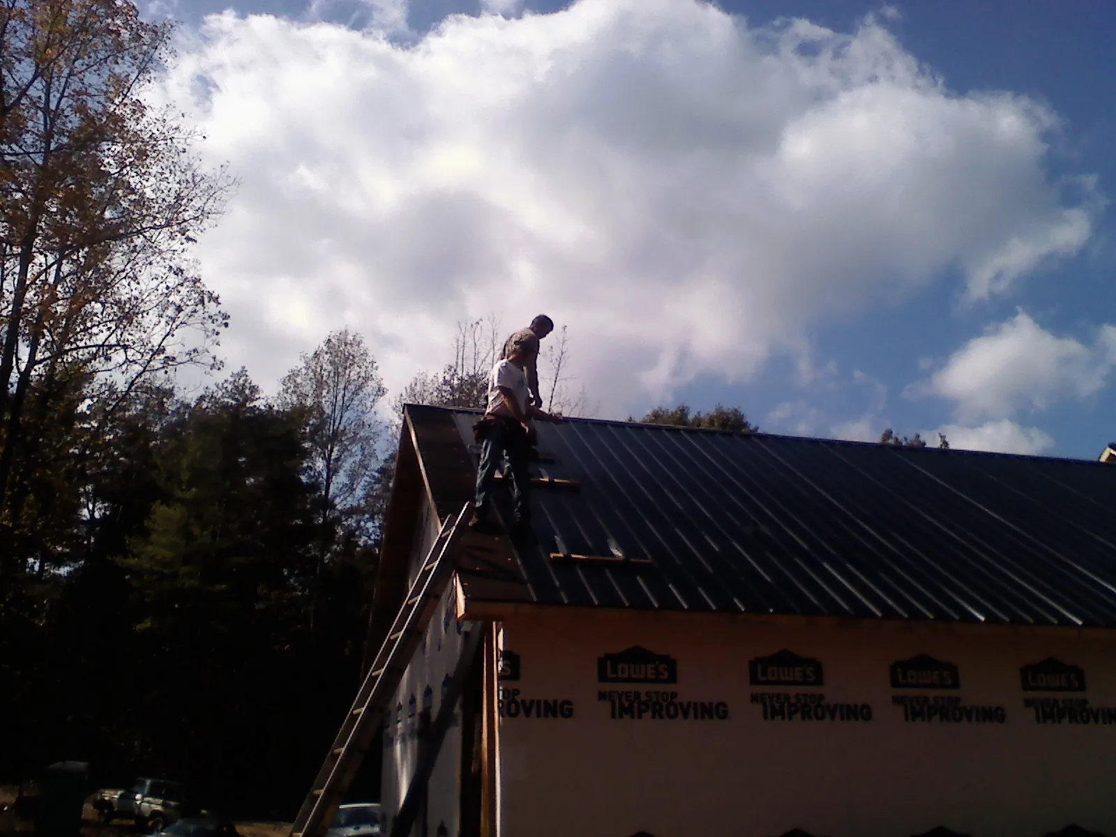 Roofer fastening dark metal panels high against a cloudy sky, from a Roof Inspection job in Glade Spring