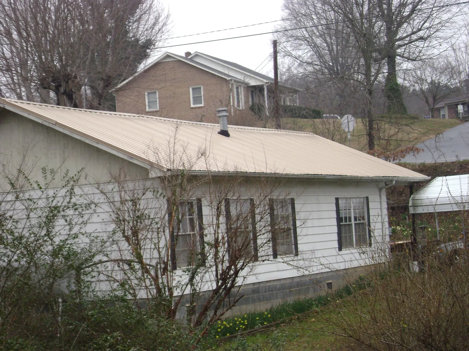Tan metal roof on a white sided house set into a hillside — Commercial Roofing by Roofing Brothers in Glade Spring